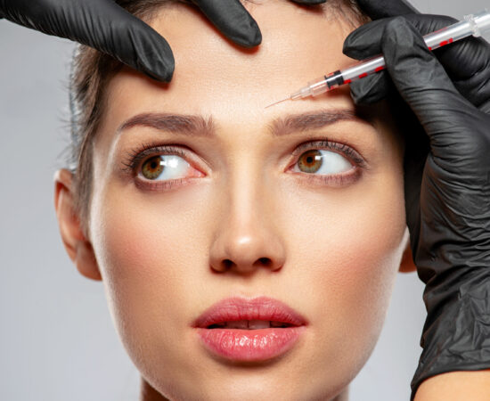 Young caucasian woman getting botox cosmetic injection in a forehead. Beautiful woman gets botox injection in her face. Adult girl gets cosmetic injection of botox in a clinic. Beauty treatments